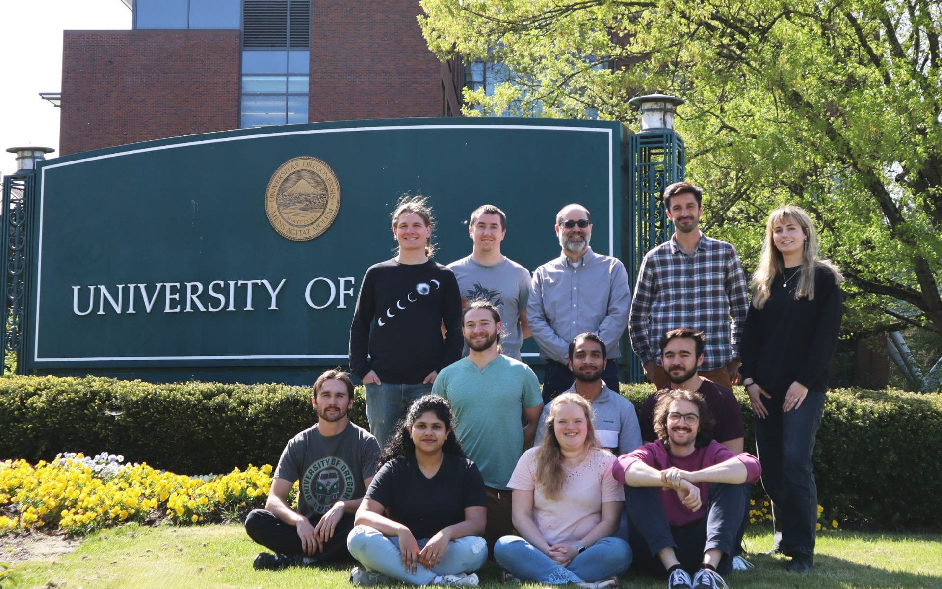 Group of electrochemistry researchers sitting and standing on the lawn in front of the University of Oregon sign